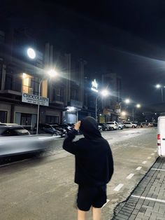 a person standing in the middle of a street at night taking a photo with his cell phone