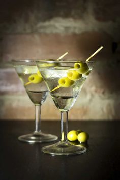 two martini glasses with olives in them