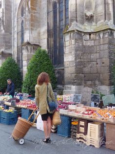 a woman is walking down the street with a cart full of fruits and vegetables in front of an old building