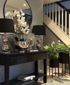 a black table with two lamps and some flowers on it in front of a staircase