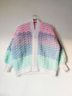 a multicolored knitted sweater hanging on a white wall next to a hanger