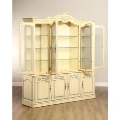 a white china cabinet with glass doors and shelves on the top, in an empty room