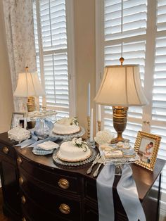 a table topped with cakes and candles next to a window covered in white sheer curtains