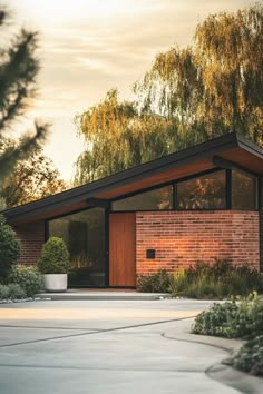 a brick house with trees in the back ground and bushes on either side of it