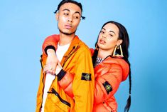 a man and woman standing next to each other in bright orange outfits on a blue background