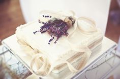 a white cake with purple flowers on top and ribbon around the edges, sitting on a table