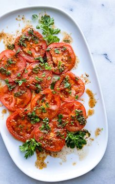 a white plate topped with sliced tomatoes and parsley on top of a marble counter