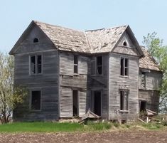 an old wooden house sitting in the middle of a field