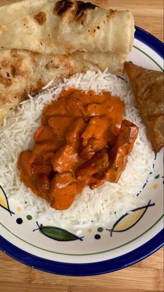 a plate topped with rice and meat covered in sauce next to flat bread on a wooden table