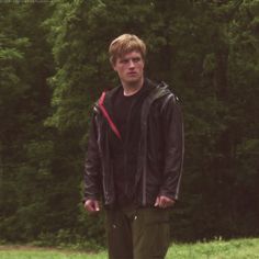 a young man standing on top of a field next to a lush green tree filled forest