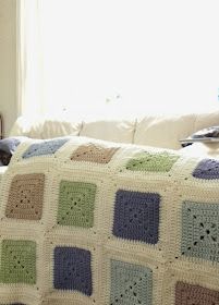 a crocheted afghan is sitting on a couch in front of a window with the sun shining through it