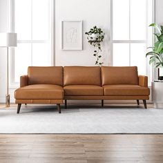 a brown leather couch sitting on top of a hard wood floor next to a window