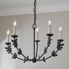 a chandelier with five lit candles hanging from it's center and leaves on the bottom