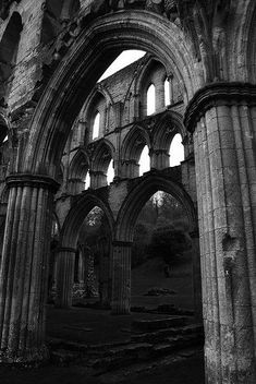 black and white photograph of the inside of an old church with stone pillars, windows and arches