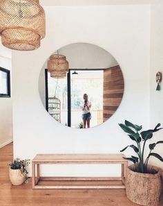 a woman standing in front of a mirror next to a bench and potted plant