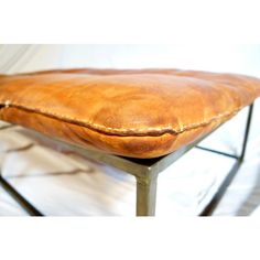 a brown leather bench with metal legs and a cushion on the seat is shown in front of a white background