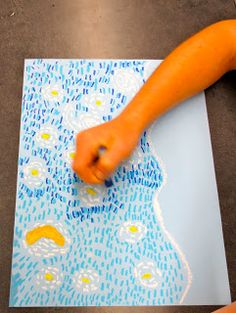 a child's hand is pointing at an art project on the paper with blue and yellow designs