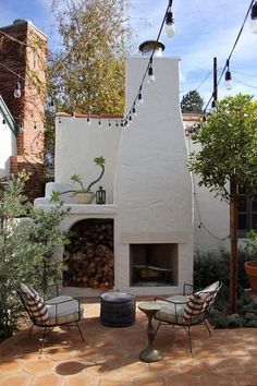 an outdoor fireplace in the middle of a patio surrounded by trees and plants, with chairs around it