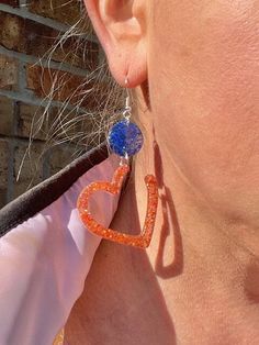 Show your Astros pride with these adorable handmade heart earrings! Crafted with resin and glitter, these earrings sparkle with the team's classic blue and orange colors. Choose from pierced or clip-on styles for a comfortable fit that works best for you. These heart earrings are perfect for game days, team events, or just whenever you want to add a pop of Astros spirit to your look. They also make a thoughtful gift for any Astros fan in your life. Let your love for the team shine bright with th