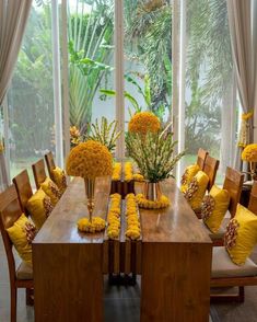 a wooden table topped with lots of yellow flowers next to a window covered in curtains