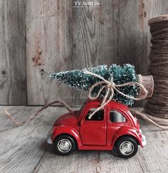 a small red car with a christmas tree on it's roof is parked in front of a spool of twine