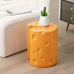 an orange stool with a potted plant on it in front of a white couch