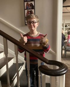 a young boy is giving the thumbs up sign while standing at the bottom of stairs