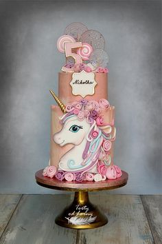 a three tiered cake decorated with pink icing and a unicorn's head