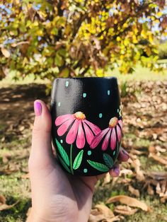 a hand holding a painted cup in front of a tree