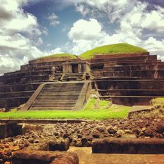 an ancient structure with steps leading up to it and grass growing on the ground below