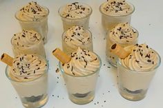 six dessert cups with whipped cream and chocolate sprinkles in them on a white surface