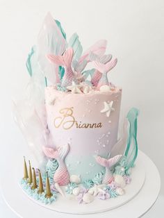 there is a pink and blue cake with mermaid decorations on the top, along with other items