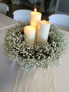 three white candles are sitting in a centerpiece with flowers and baby's breath