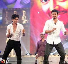 two men in white shirts and black pants on stage with one man holding a microphone