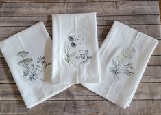 three embroidered tea towels with flowers on them sitting on top of a wooden table next to each other