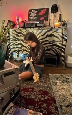 a woman sitting on the floor playing an electric guitar in front of a zebra print wall