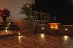 an outdoor fire pit lit up at night with lights on the steps and potted plants