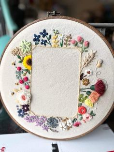 an embroidered frame with flowers and leaves is on a table next to some papers, scissors and other items