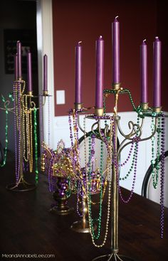 there are many candles on the table with beads and chains hanging from each candle holder