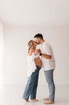 a man and woman kissing while standing next to each other in front of a white wall