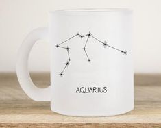 the aquariusus zodiac sign on a white coffee mug sitting on a wooden table