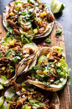 three tacos with meat, lettuce and other toppings on a cutting board