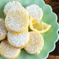 lemon cookies with powdered sugar are on a green plate next to sliced lemons