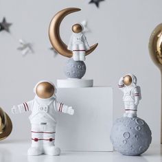 two small astronaut figurines standing on top of a white block next to gold and silver stars