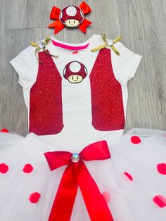 a white and red dress with bows on the headband is sitting in front of a wooden floor