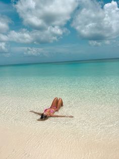 a woman laying on top of a sandy beach under a blue sky with white clouds