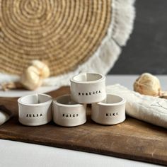 four white ceramic bowls sitting on top of a wooden cutting board next to garlic cloves