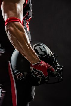 a football player holding his helmet and ball in one hand while standing against a black background