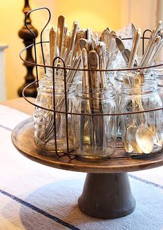 there are many mason jars and spoons in the holder on the table with lights behind them