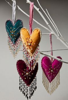 three heart shaped ornaments hanging from a twig with beads and tassels on them